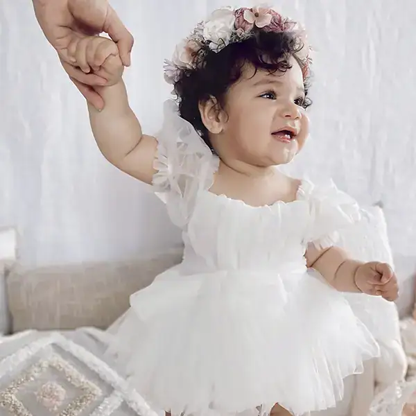 Niña con vestido blanco y corona de flores, luciendo elegante y adorable.